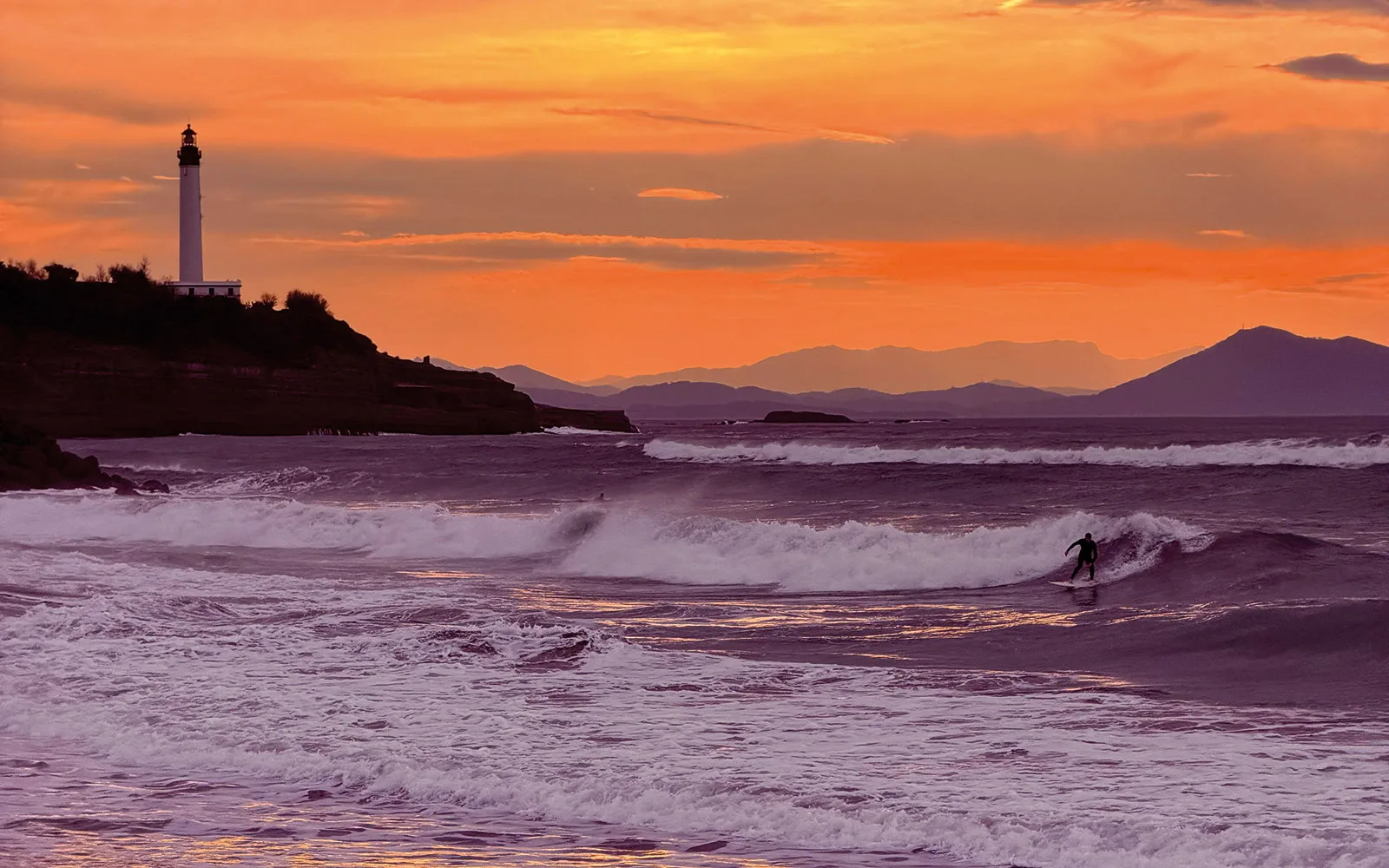 Le phare de Biarritz au coucher de soleil et un surfeur sur la vague